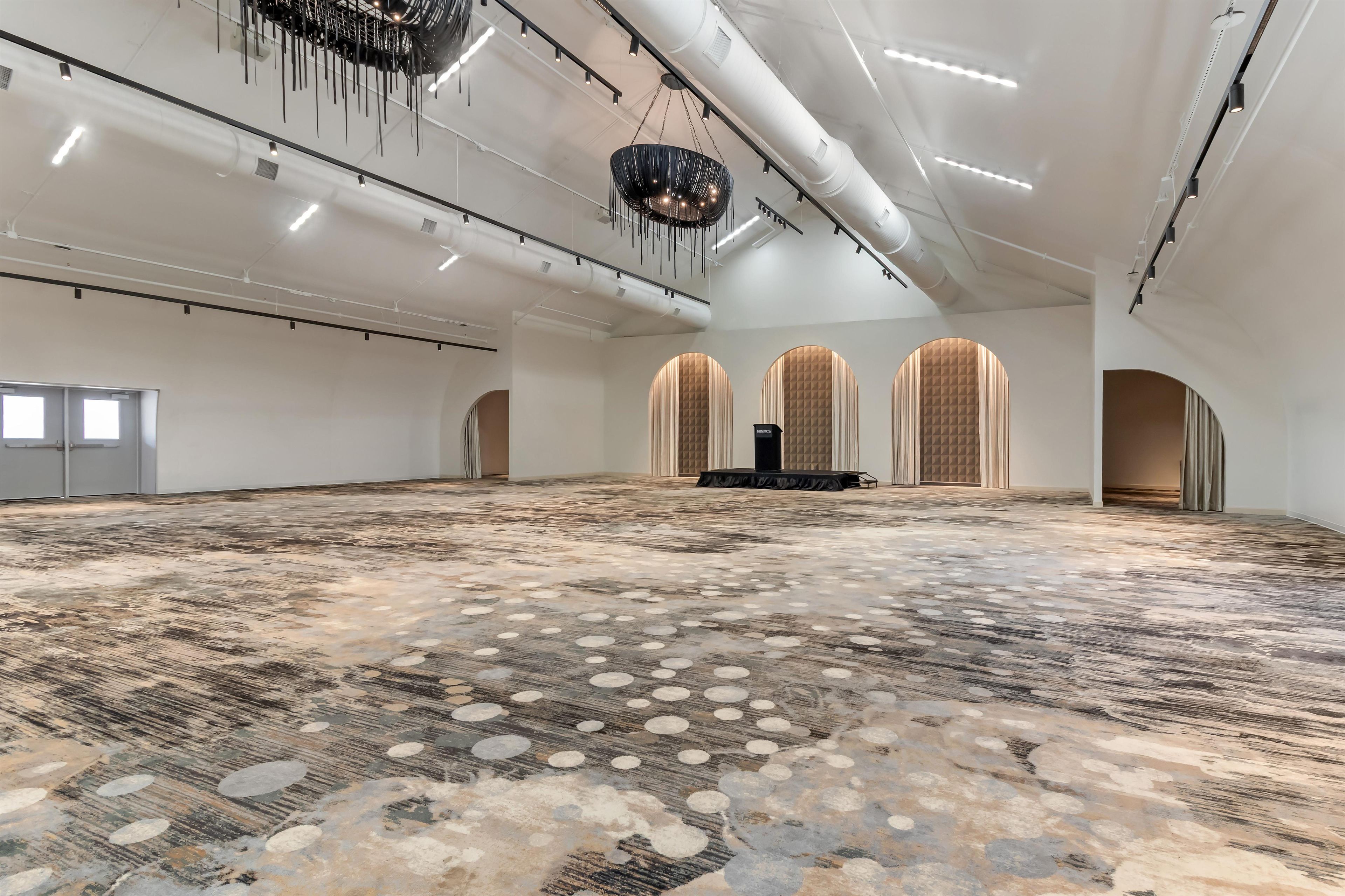 A spacious hall with a patterned floor, a central stage, and a modern chandelier.