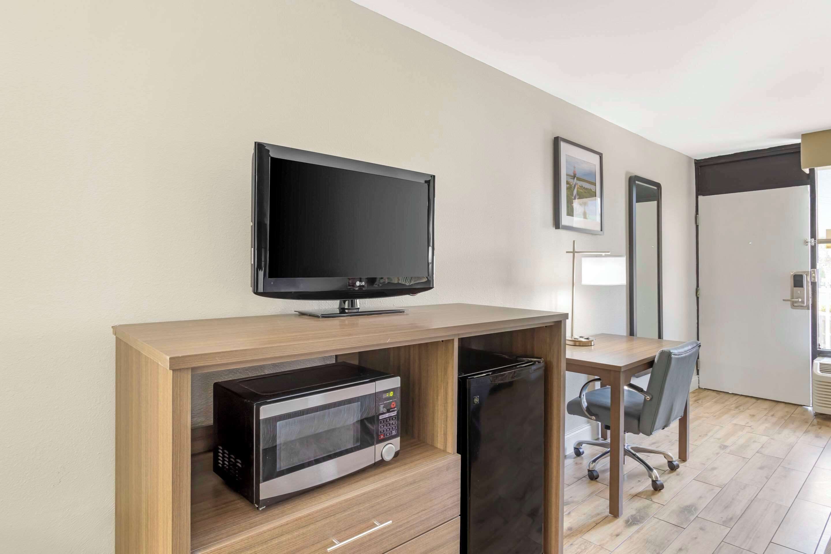 Ein modernes Hotelzimmer mit Schreibtisch aus Holz, Flachbildfernseher, integriertem Mikrowellenherd und Kühlschrank.