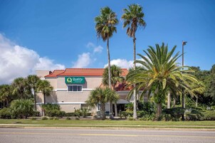 Un hotel con techo de tejas rojas, palmeras y un letrero que dice 'Quality Inn & Suites'.