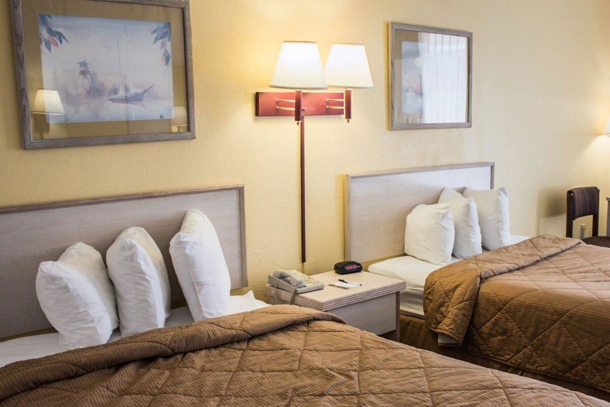 Habitación de hotel con dos camas, una mesita de noche con lámpara, teléfono y un cuadro en la pared.