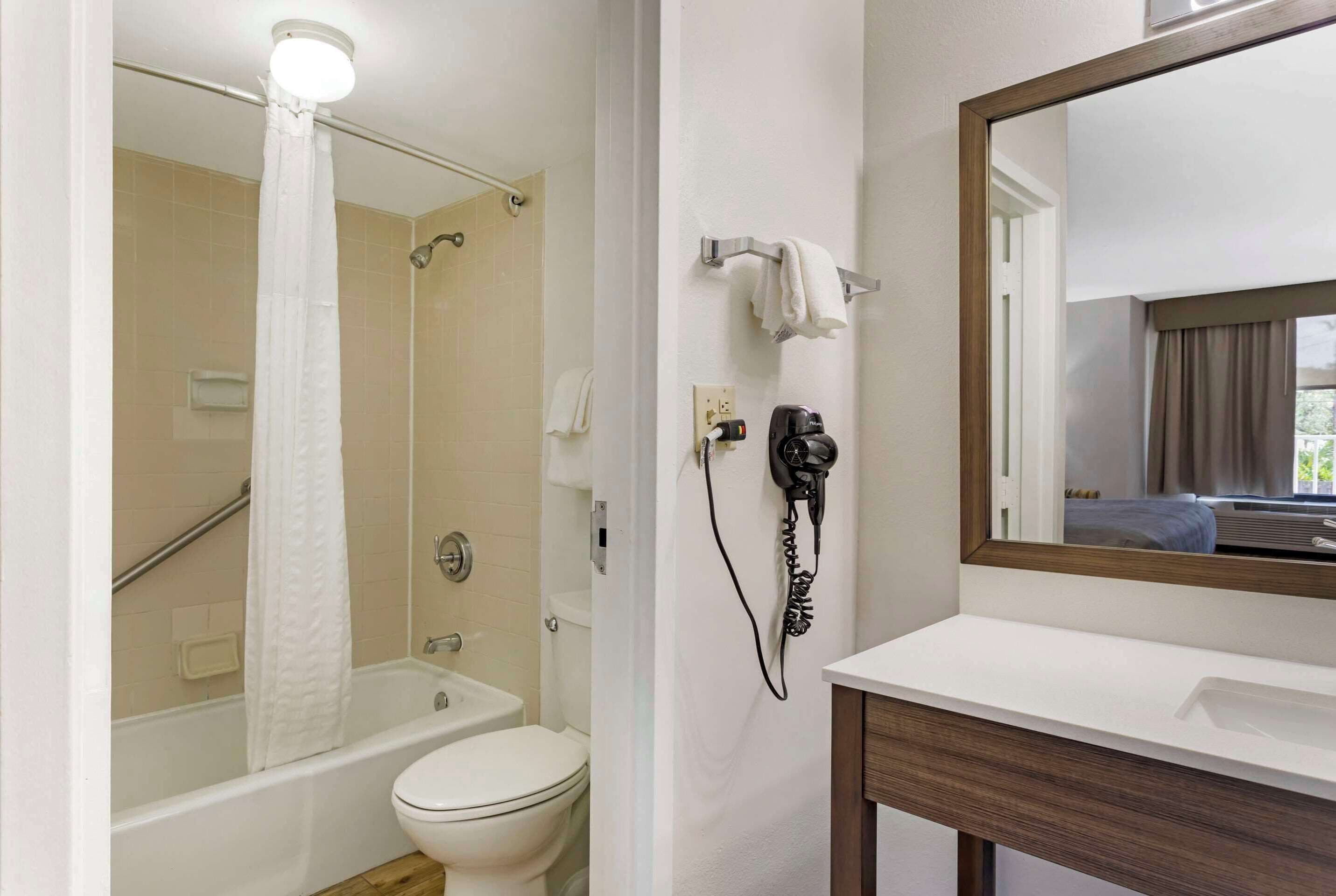A bathroom with a bathtub, toilet, and a hairdryer on the wall.
