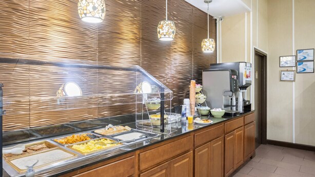 A buffet setup with various food items, a coffee machine, and a water dispenser. - Quality Suites Hickory South (Hickory)