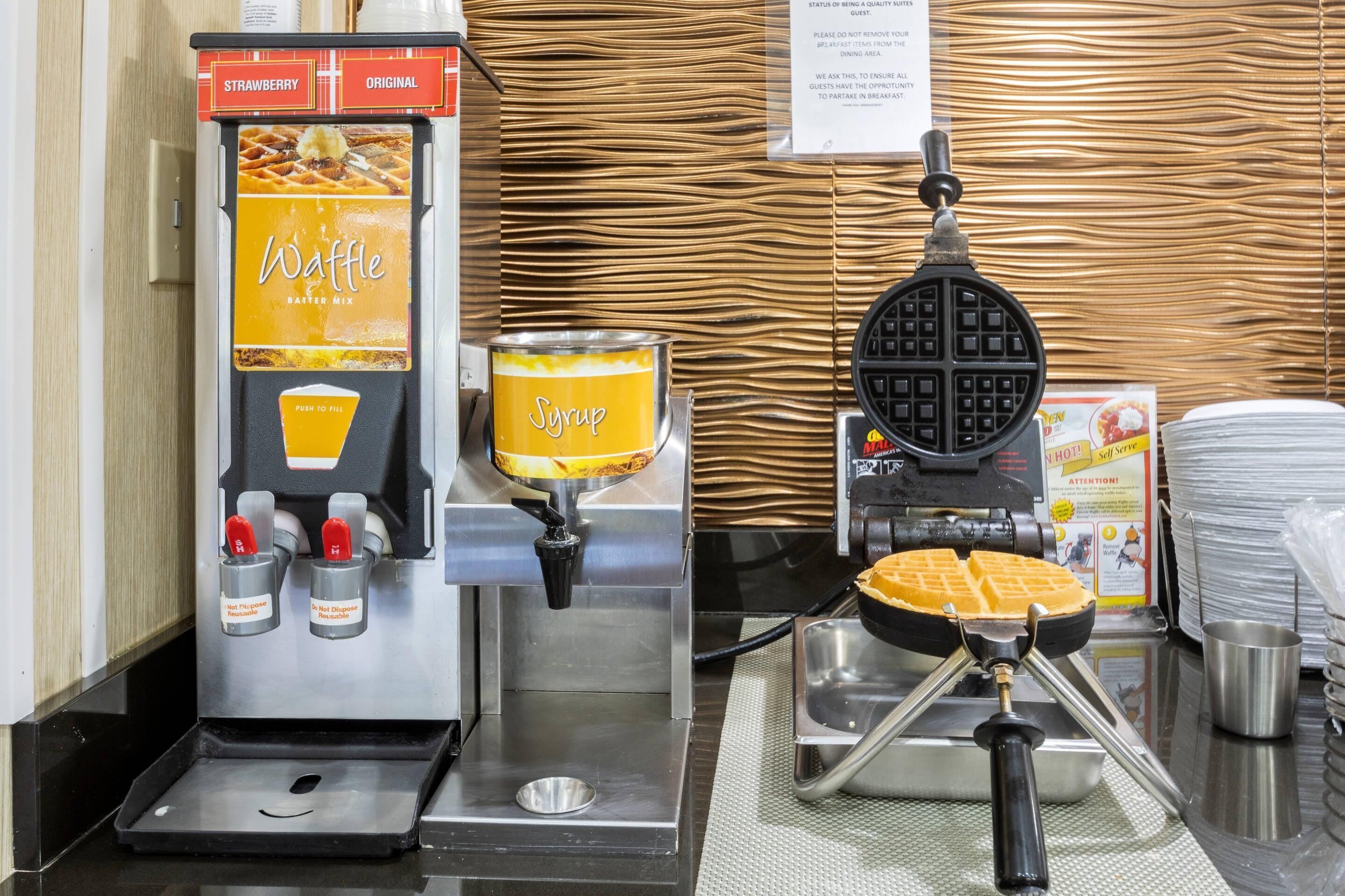 Una máquina para hacer gofres, dispensador de jarabe y estación de gofres en una cocina.