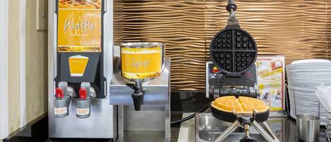 A waffle maker, syrup dispenser, and waffle station in a kitchen area.
