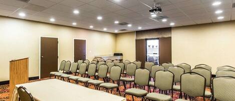 A conference room with a long table, rows of chairs, a podium, and a projector screen.