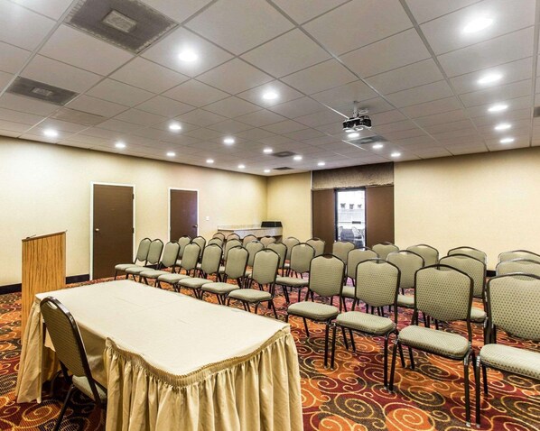 A conference room with a long table, rows of chairs, a podium, and a projector screen.