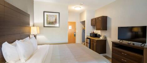 Habitación de hotel con una cama grande, televisión, escritorio con lámpara y kitchenette.