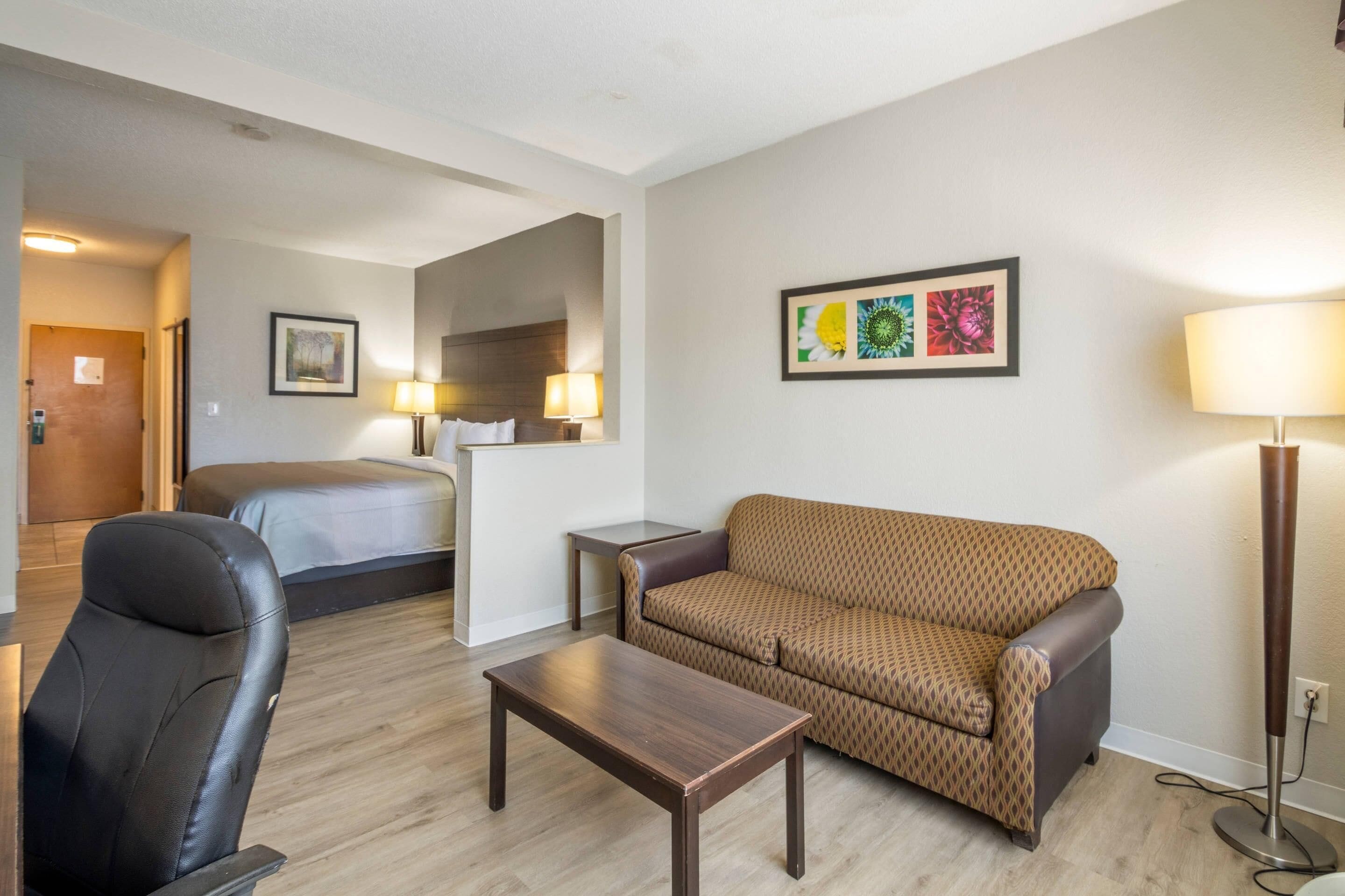 Une chambre d’hôtel avec un lit, un canapé, une chaise, une petite table et une lampe.
