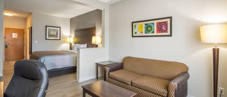 Une chambre d’hôtel avec un lit, un canapé, une chaise, une petite table et une lampe.
