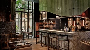 Uma área de bar com bancada de mármore, vários bancos e uma variedade de garrafas.