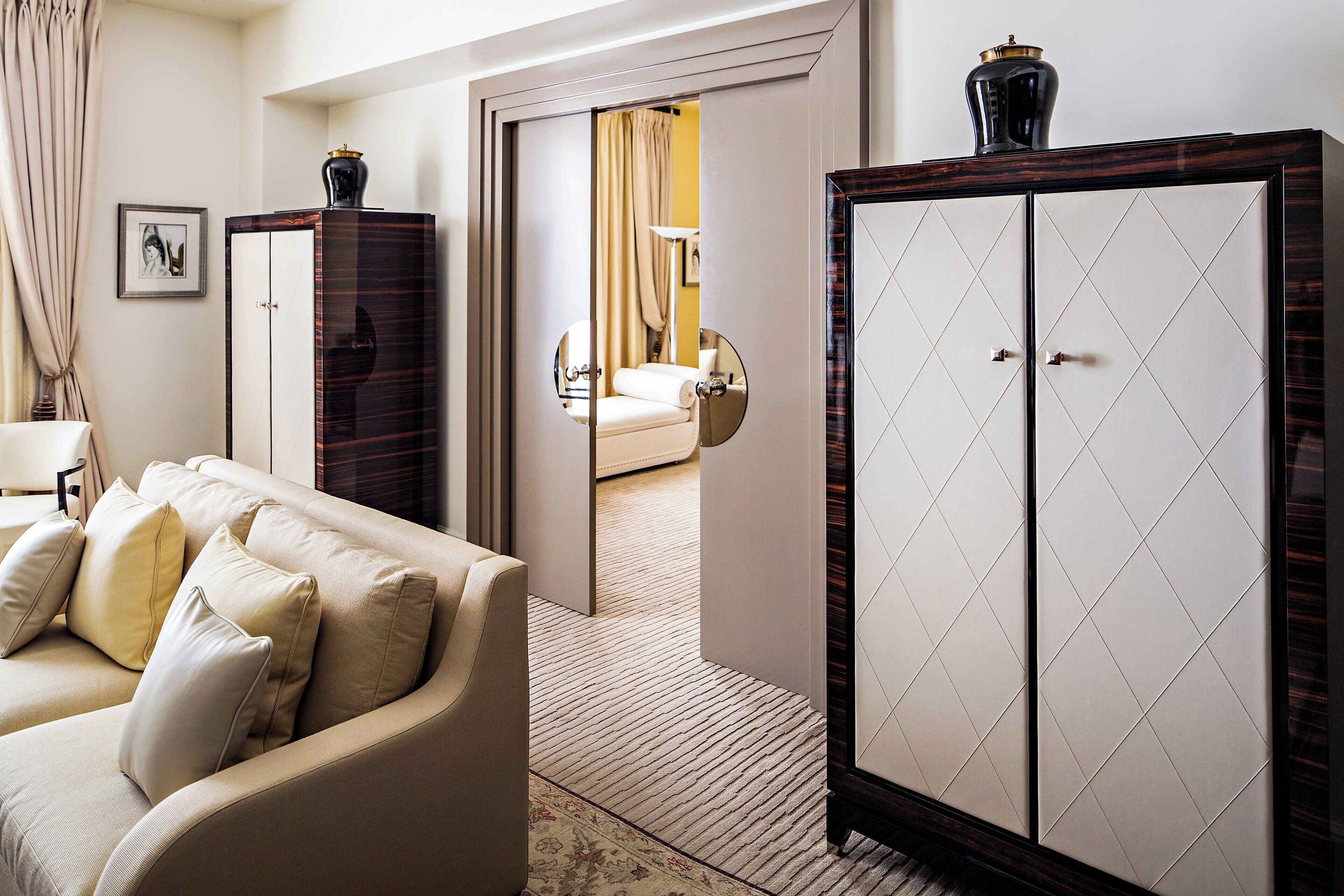Een hotelkamer met een beige bank, een grote garderobe en een spiegel die de badkamer weerspiegelt.