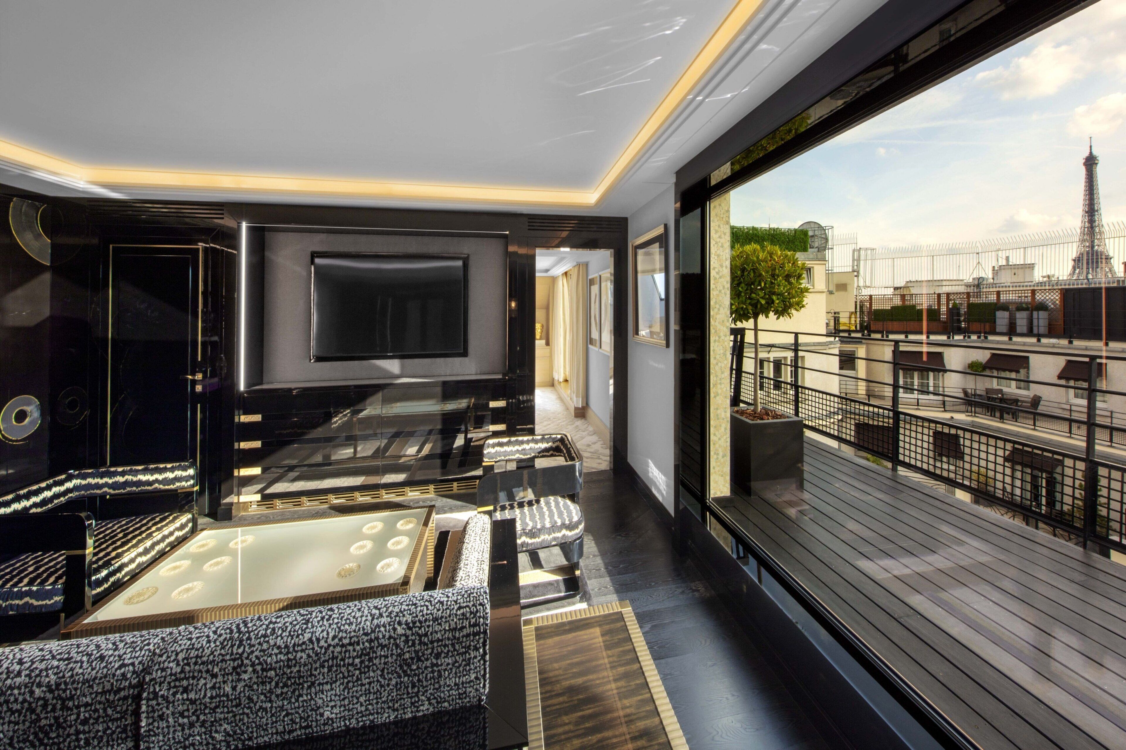 A modern interior with a large flat-screen TV, plush seating, and a balcony with a city view.