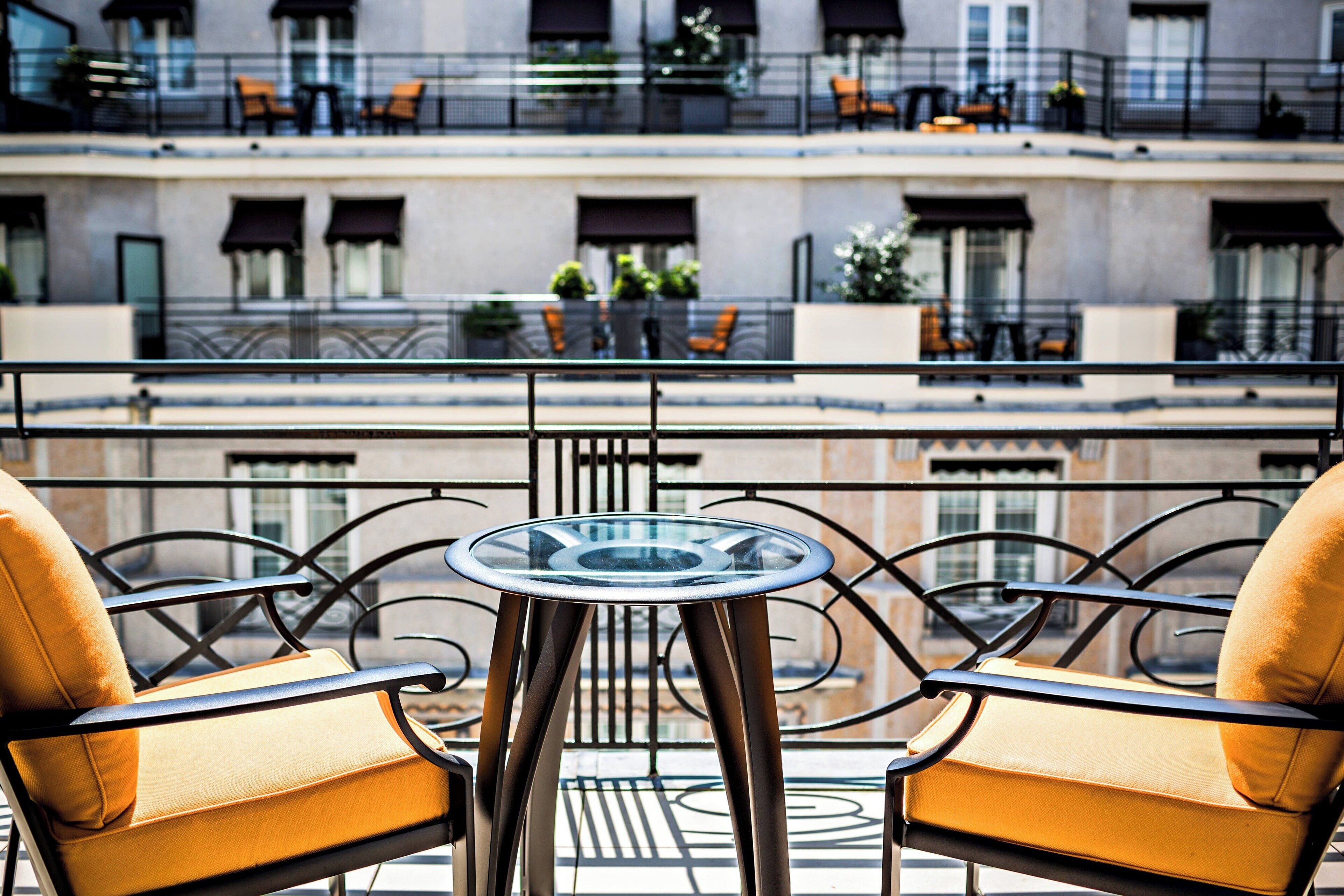 A balcony with a glass table and two yellow chairs, overlooking a building with multiple balconies and outdoor seating.