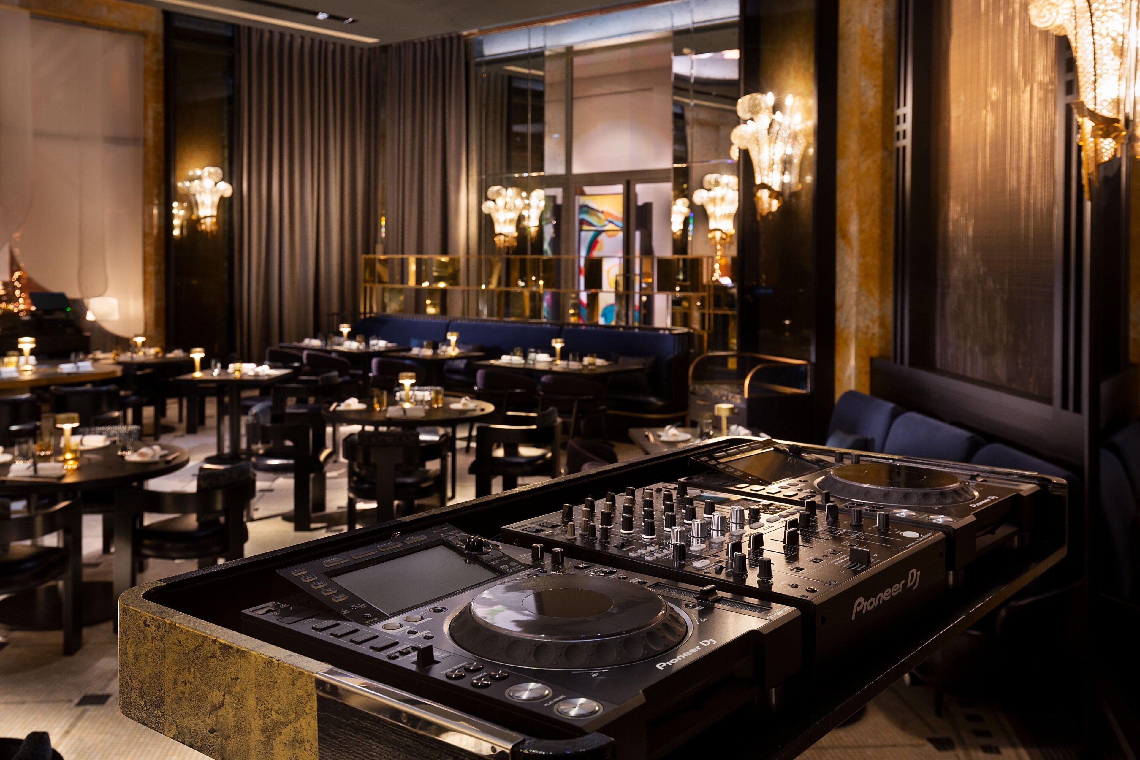 A modern interior with DJ equipment, tables, chairs, and ambient lighting.