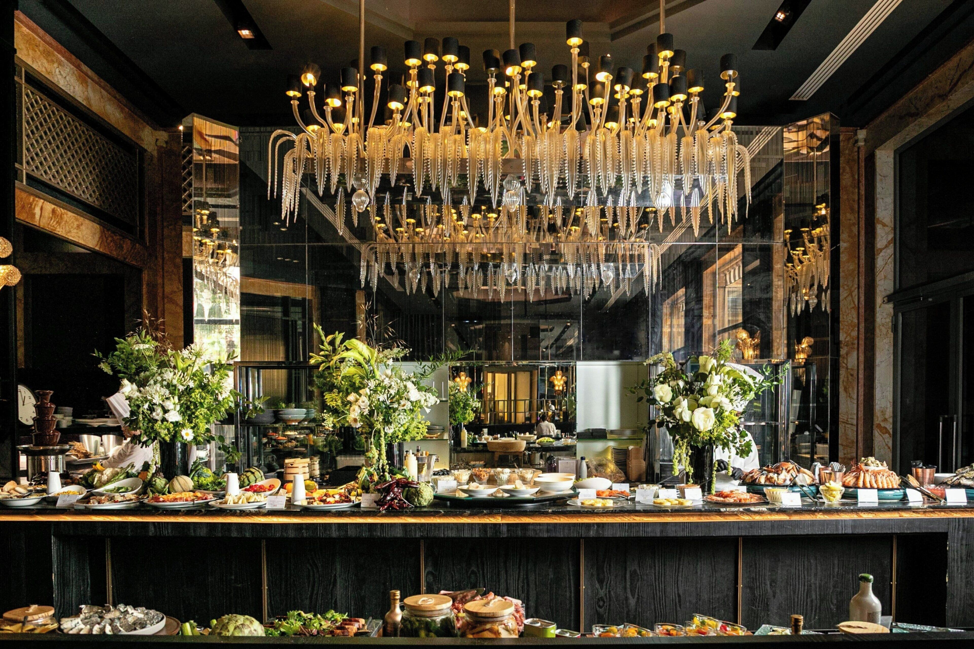 Ein luxuriöser Essbereich mit einem prächtigen Kronleuchter, mehreren floralen Tischdekorationen und einem reichhaltigen Buffet.