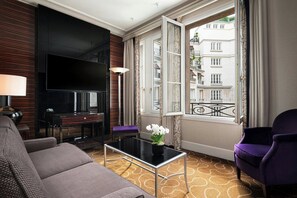 Une chambre d  ’hôtel moderne dotée d’une grande télévision à écran plat, d’un canapé, d’une table basse agrémentée d’un vase de fleurs et offrant une vue sur la ville grâce à une grande fenêtre.