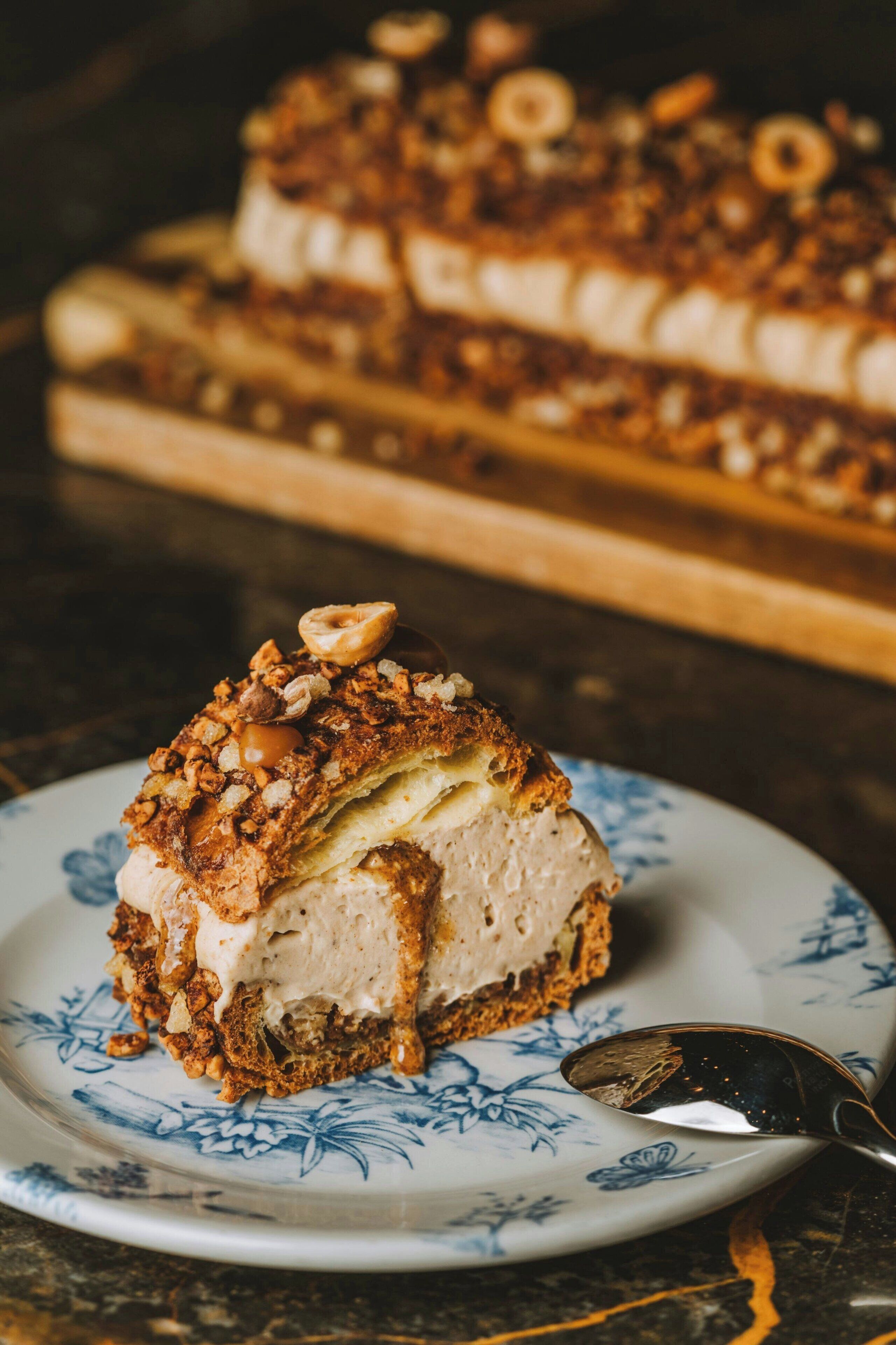 A slice of cake on a plate with a spoon, and a whole cake in the background.
