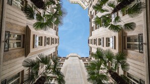 A symmetrical building facade with a central pathway flanked by palm trees, leading to a clear blue sky.