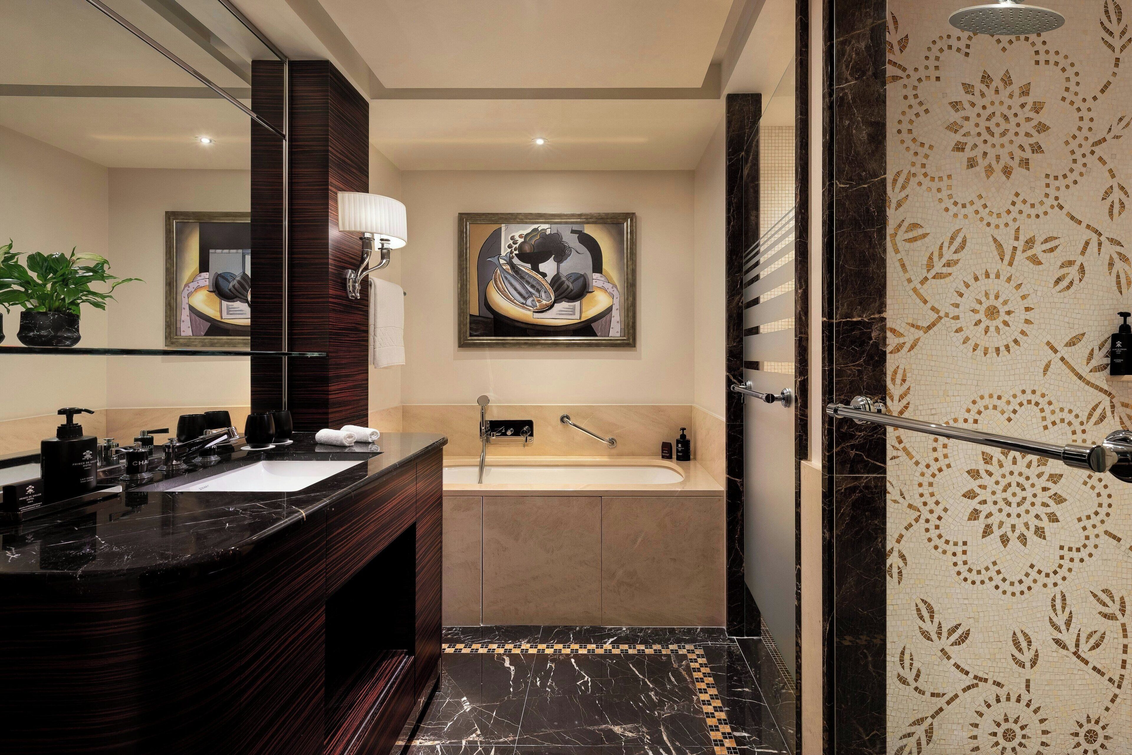 Een moderne badkamer met een zwart marmeren wastafel, een badkuip en een douche met decoratieve wand.
