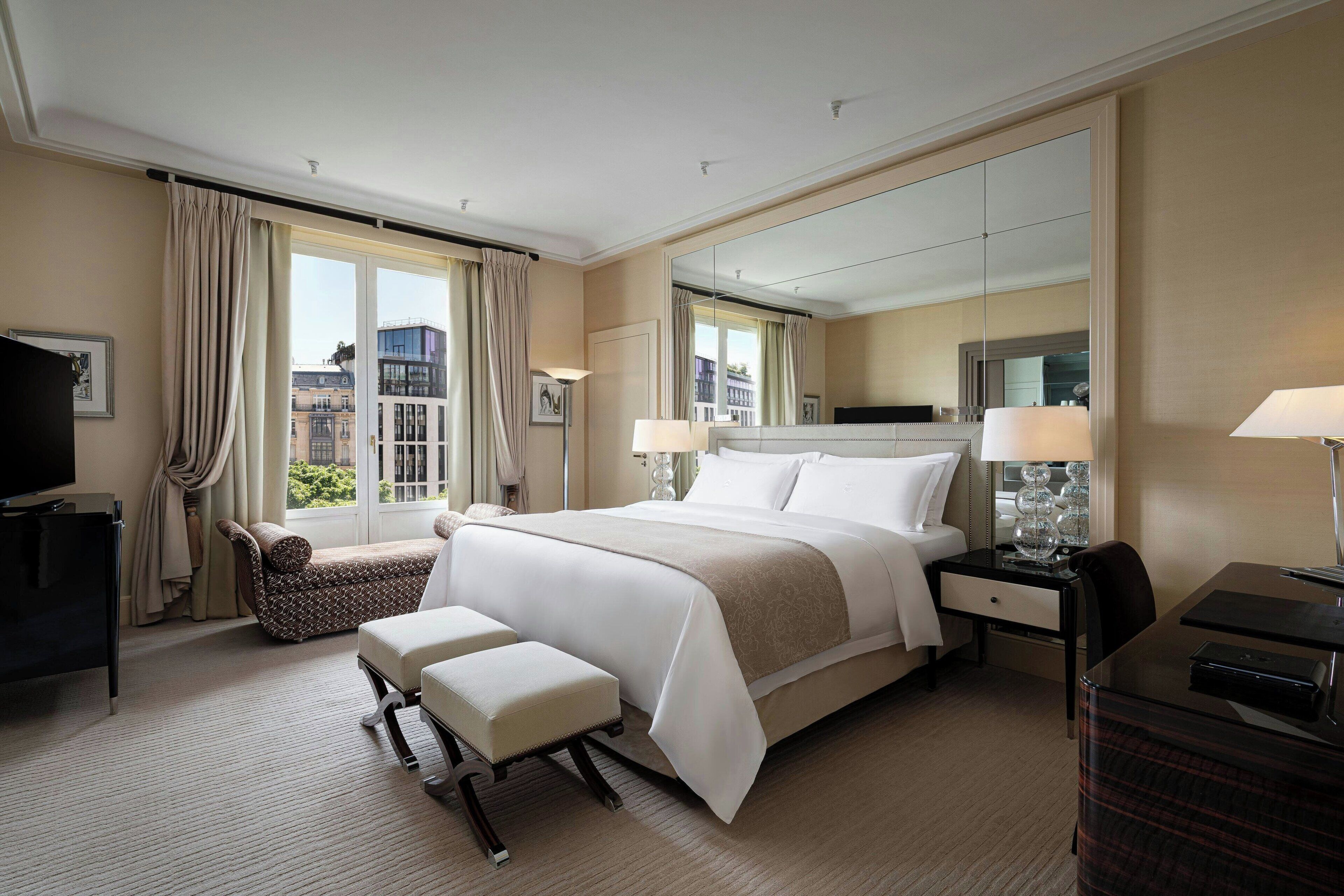 Een hotelkamer met een groot bed, een bureau, een stoel, een televisie en een raam met gordijnen.
