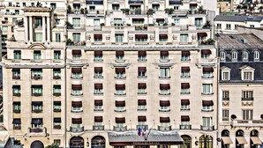 Un hotel de varios pisos con fachada clásica, con balcones adornados con plantas y una entrada destacada con un cartel.