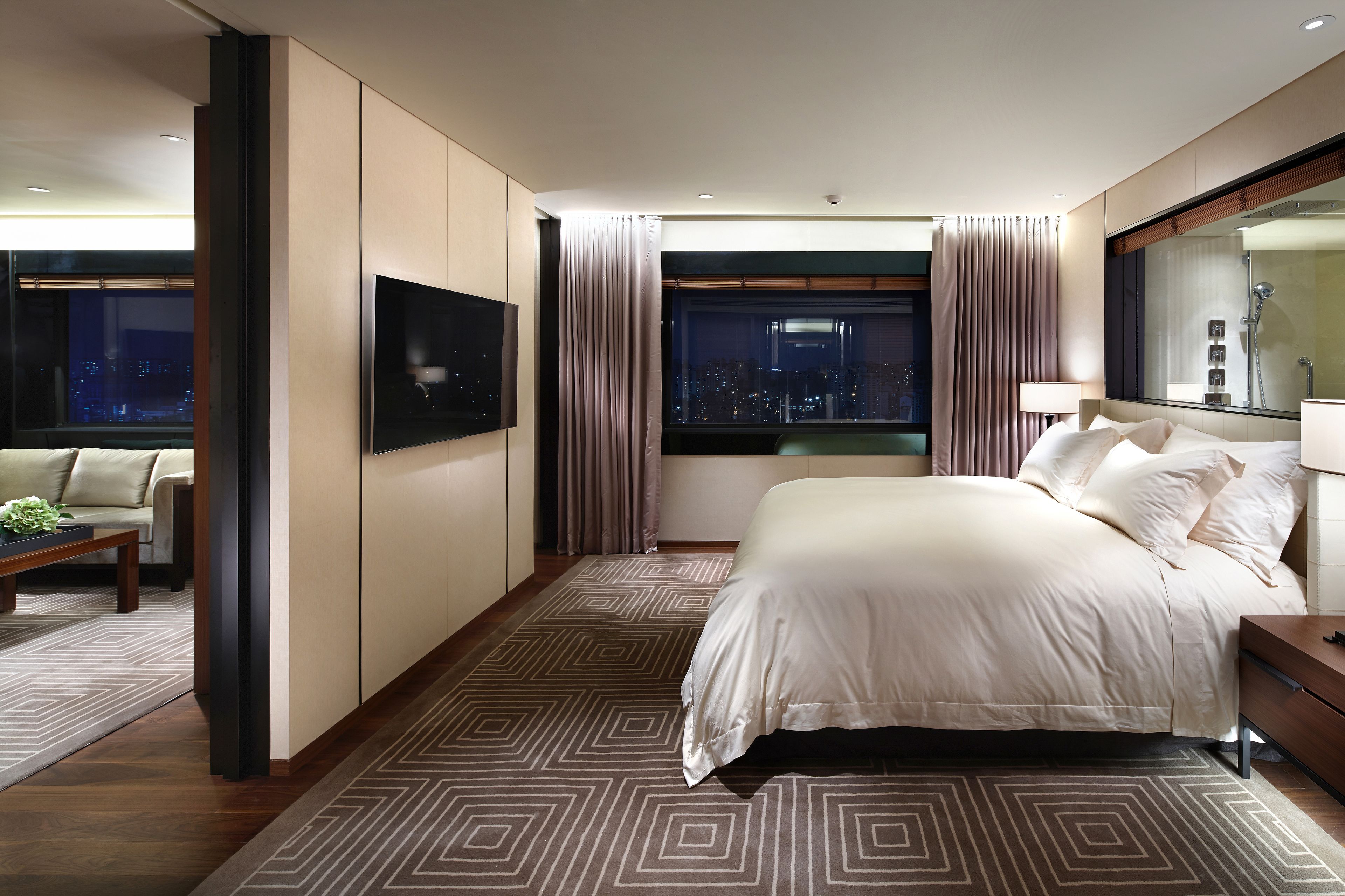 Una habitación de hotel moderna con una cama grande, vistas a la ciudad, un televisor de pantalla plana y un área de descanso con una mesa de centro.