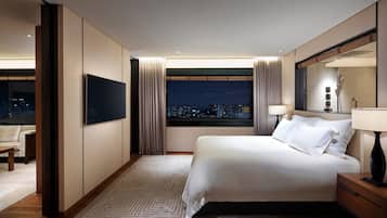 Ein Hotelzimmer mit Bett, Fernseher, Nachttisch, Lampe und Blick auf die beleuchtete Stadt.