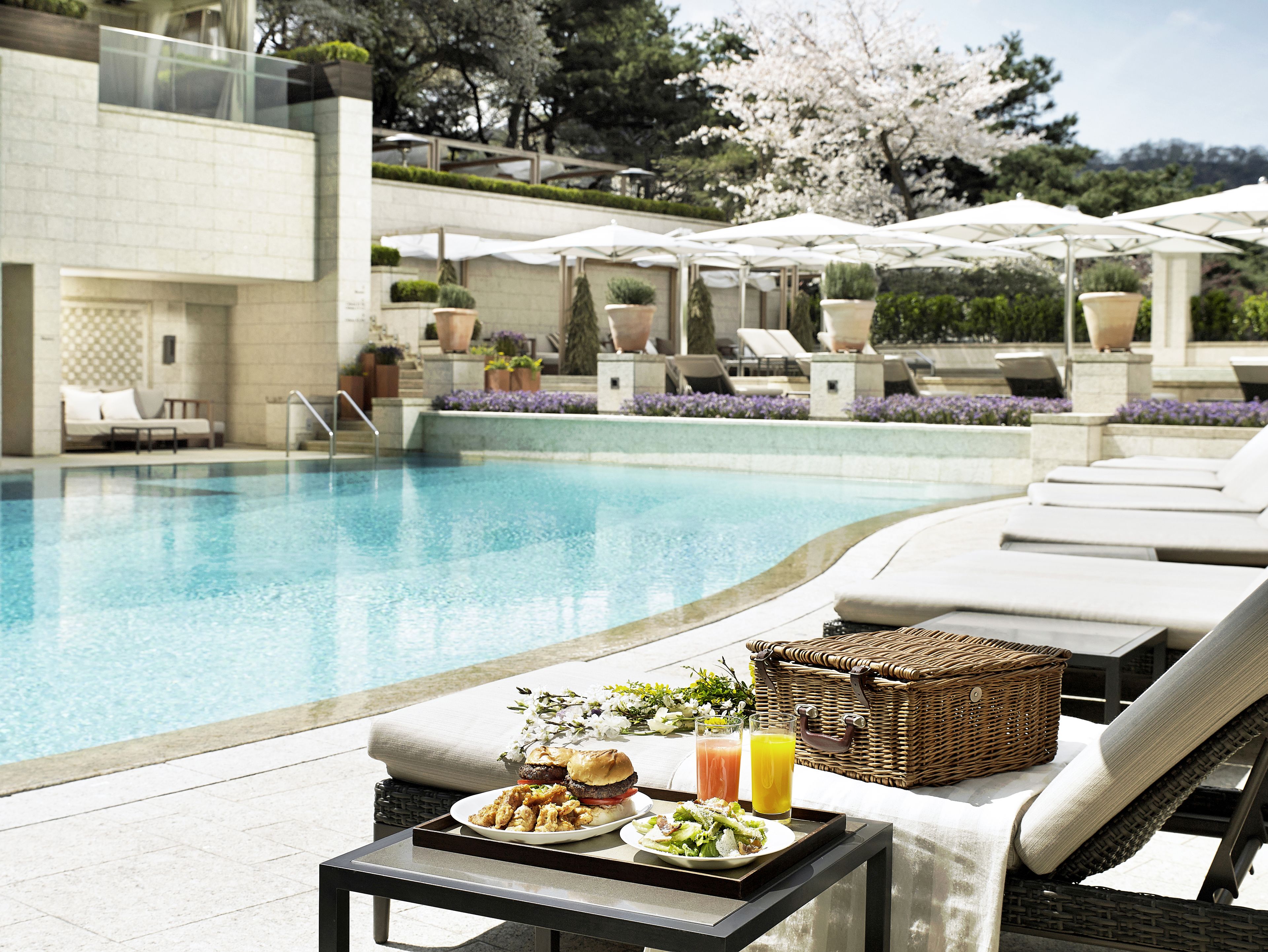 Un espacio junto a la piscina con sillas de descanso, una mesa con comida y bebidas, y vistas a la piscina.