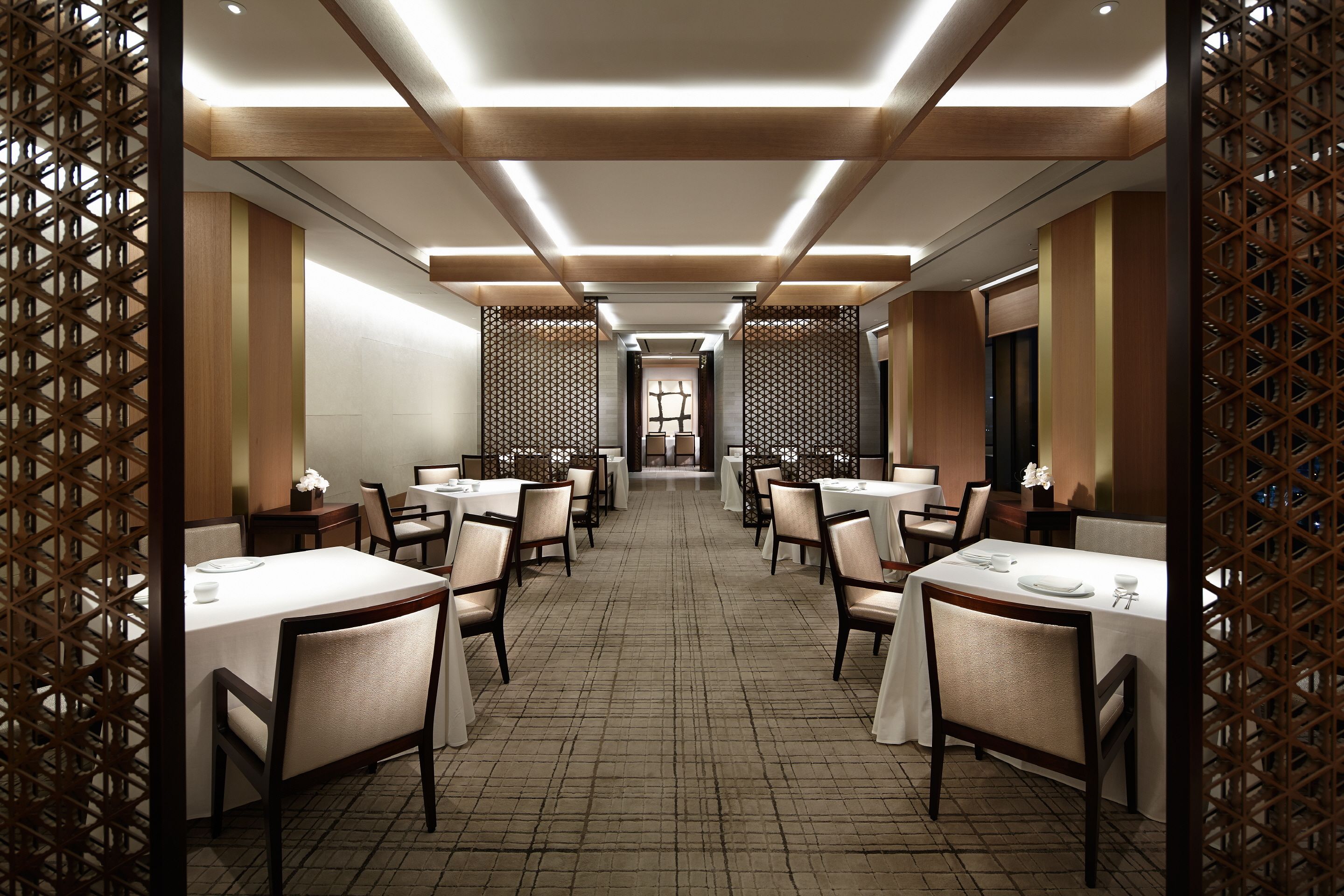 A hotel dining area with multiple tables and chairs, wooden paneling, and a tiled floor.
