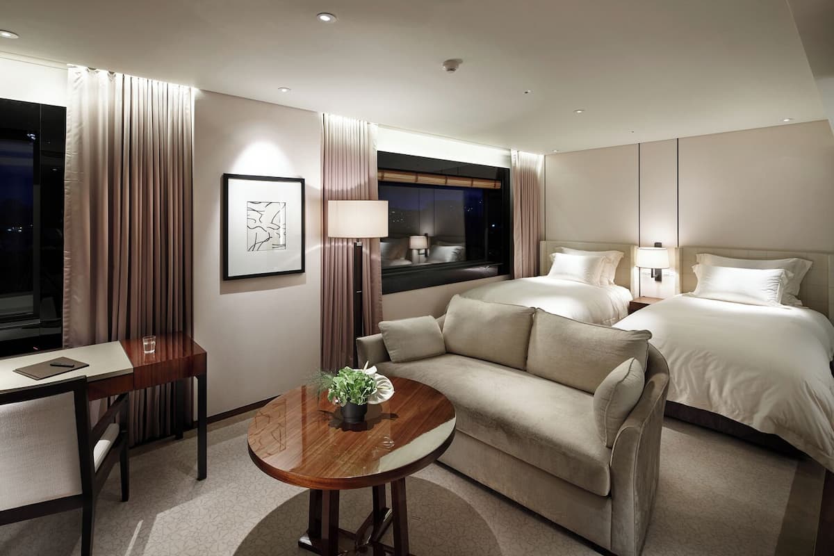 Quarto de hotel com cama, sofá, escrivaninha e uma pequena mesa com uma planta.