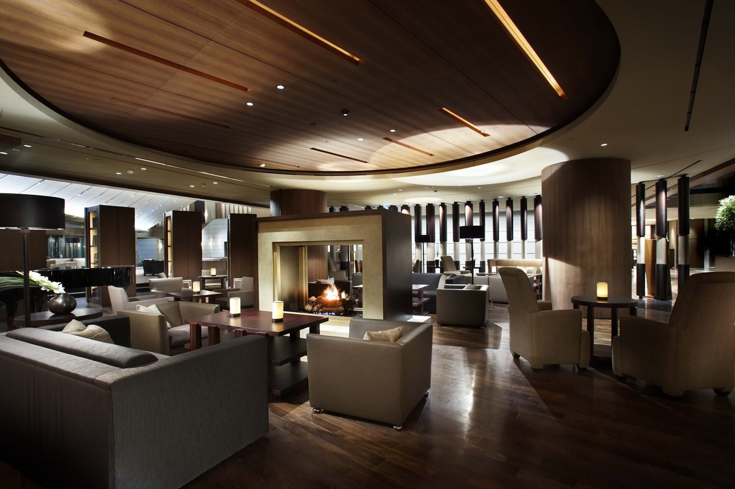 Un lobby moderno con una chimenea central, asientos cómodos y un techo de madera.