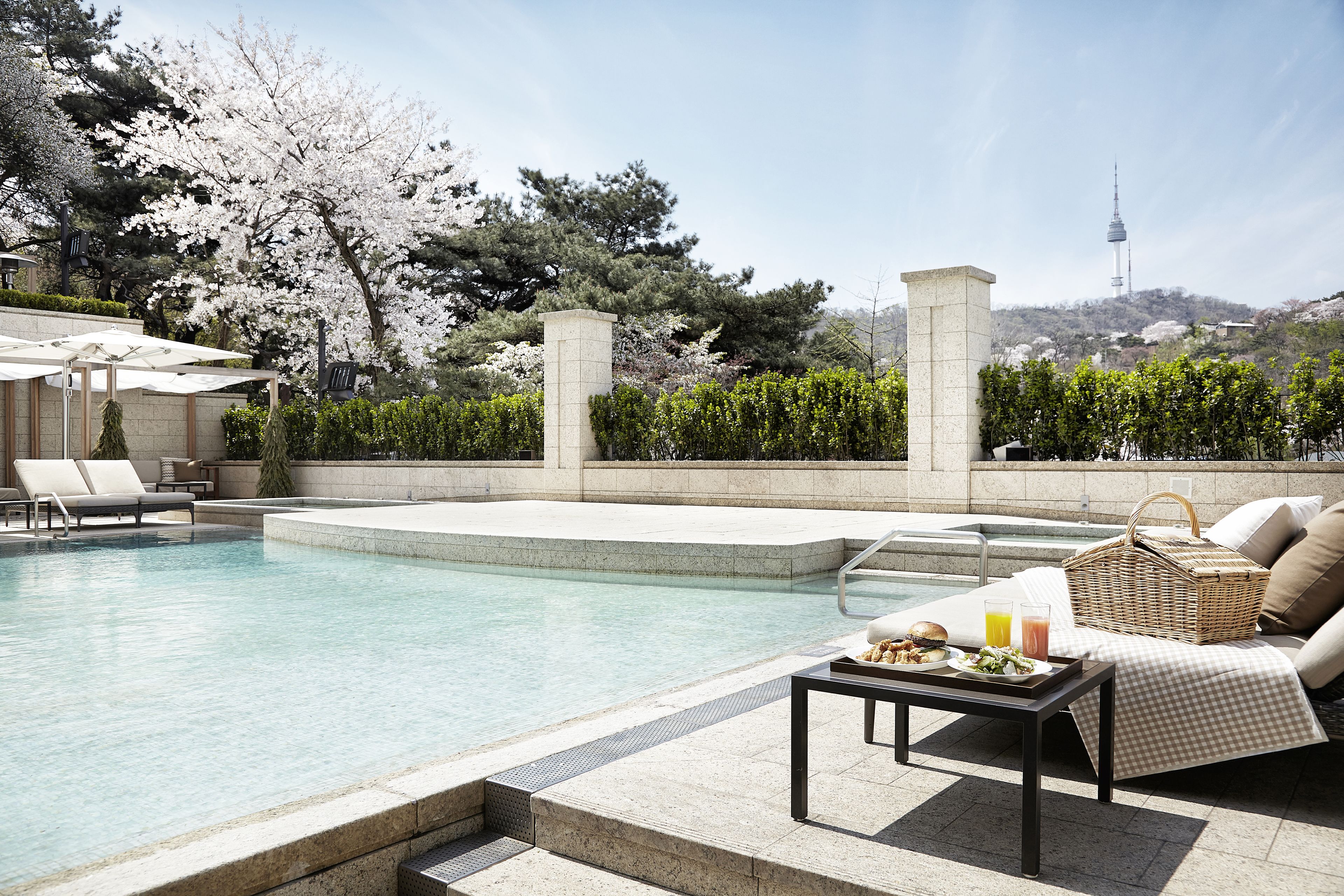 Zona de piscina con sillones de descanso, una mesa con comida y bebidas, y una vista de una torre al fondo.