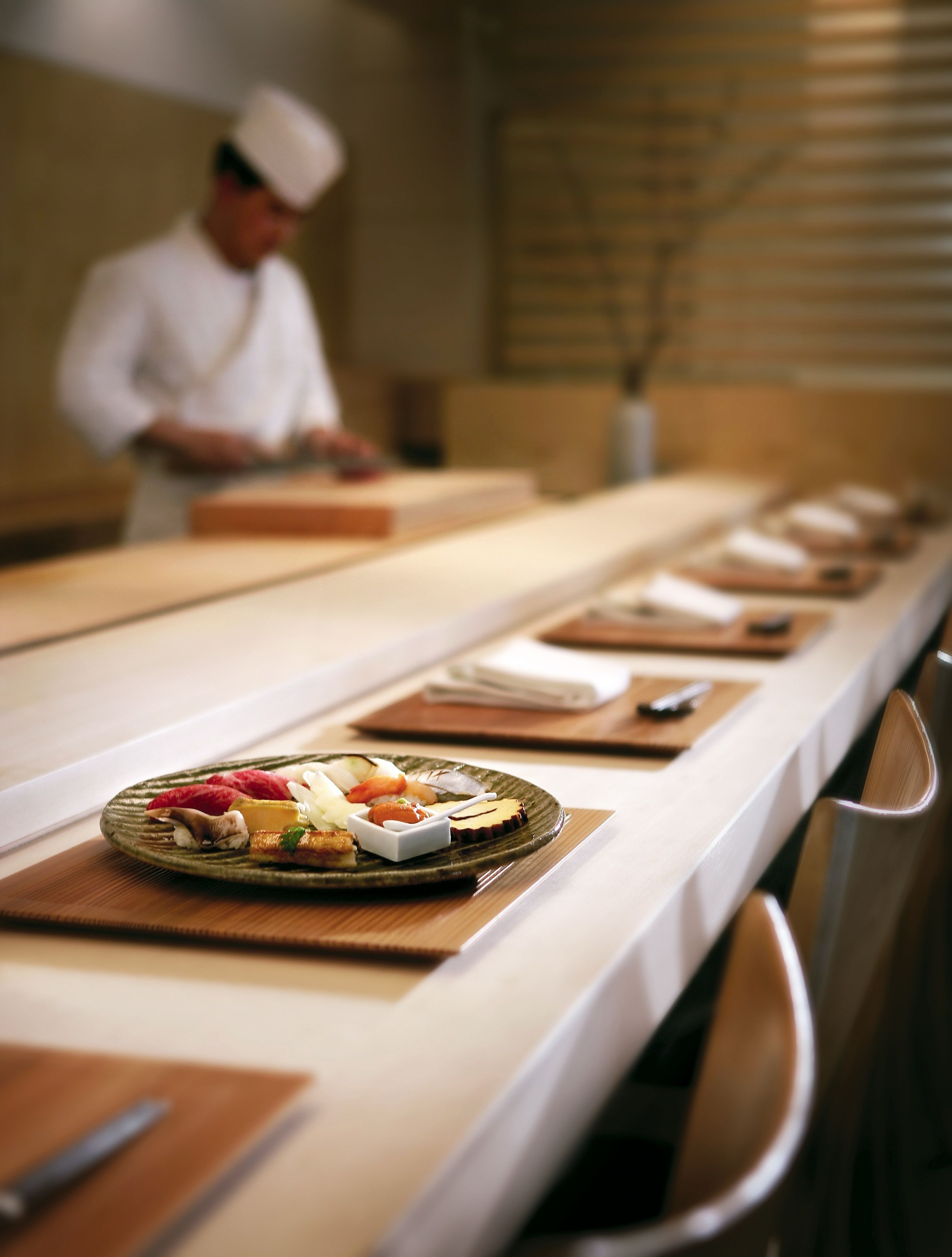A long dining table with neatly arranged plates of food, a chef in the background, and a clean, modern interior.