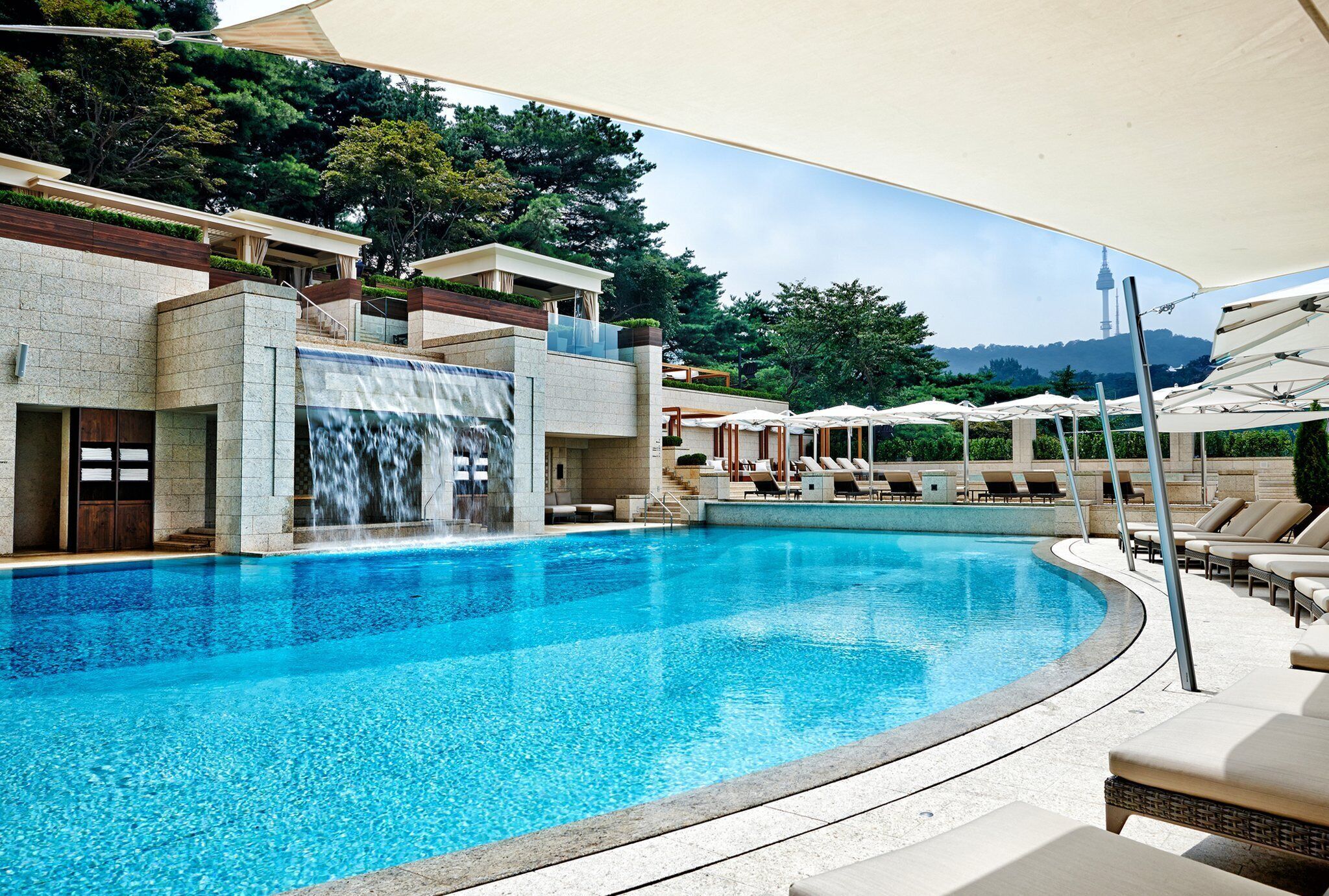 A swimming pool with a waterfall feature, lounge chairs, and umbrellas.