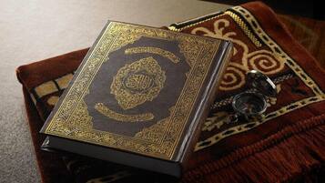 A book with ornate gold detailing on a dark cover, placed on a patterned fabric.