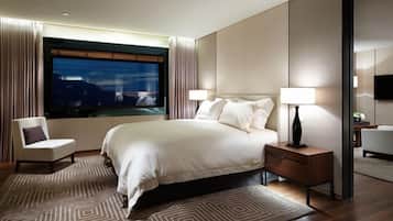 A modern hotel room with a large bed, two bedside tables, a TV, and a view of the city at night.