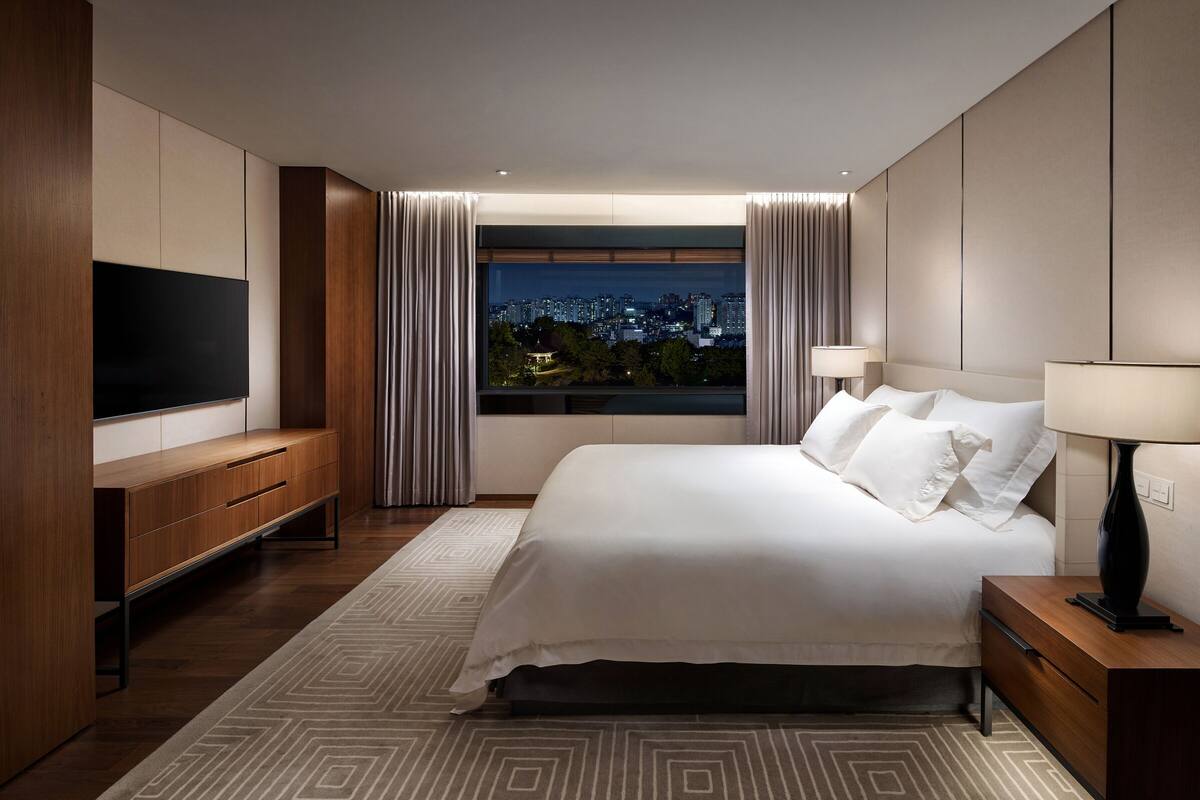 Quarto de hotel moderno com uma cama grande, televisão e vista para a cidade.