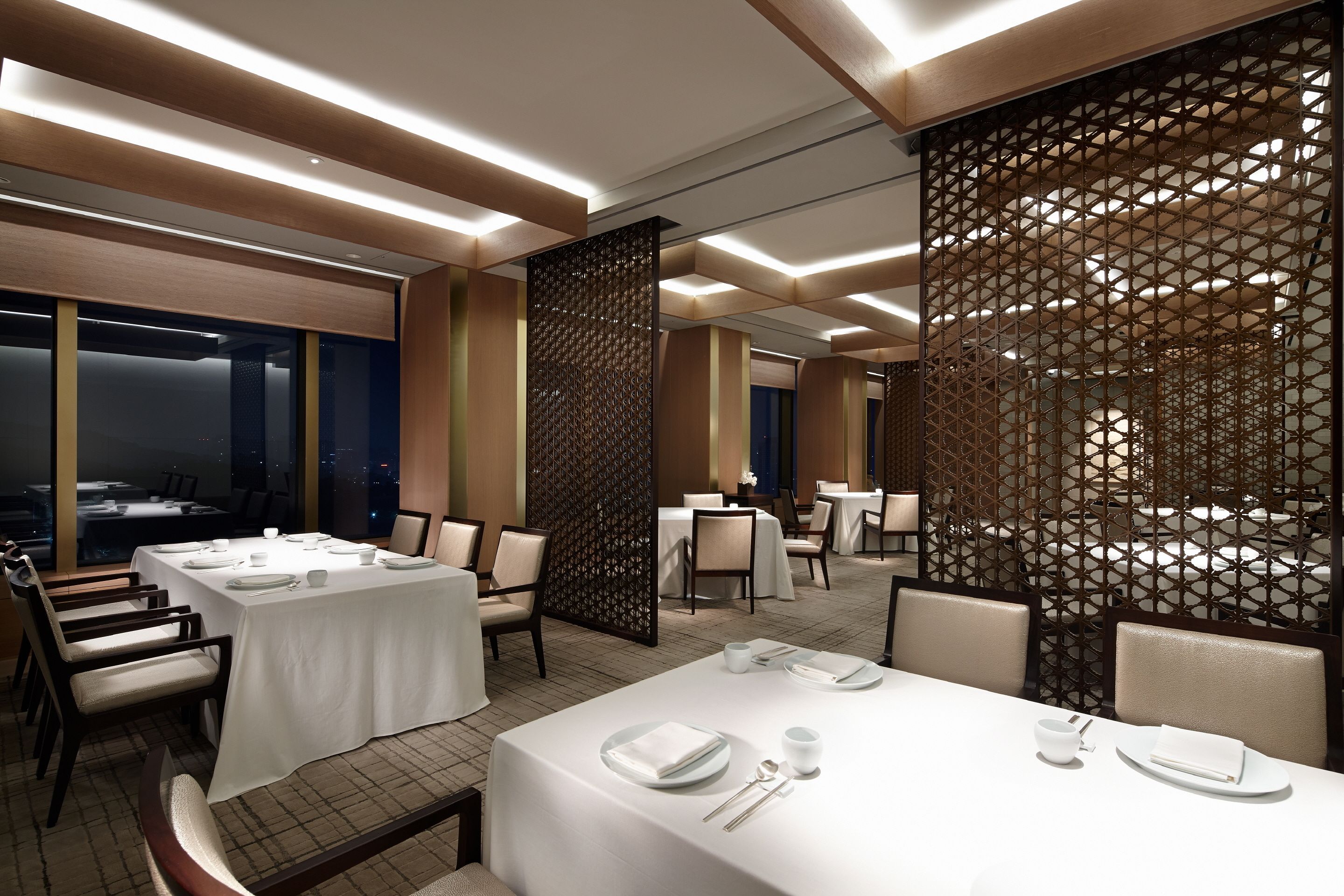 Un comedor moderno con mesas dispuestas para el servicio, techo alto con iluminación empotrada y un separador decorativo.