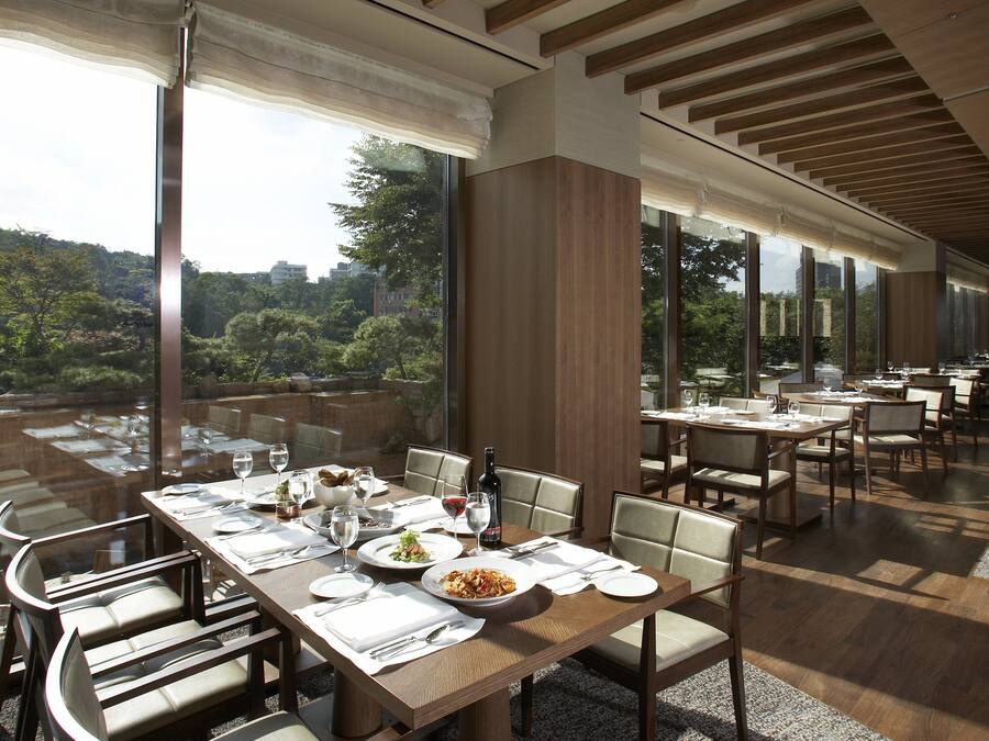 A restaurant with a long table set for dining, large windows offering a view of the outdoors, and a modern interior design.