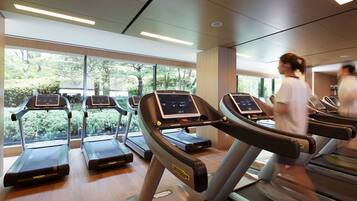A gym with treadmills and a large window with a view of greenery.