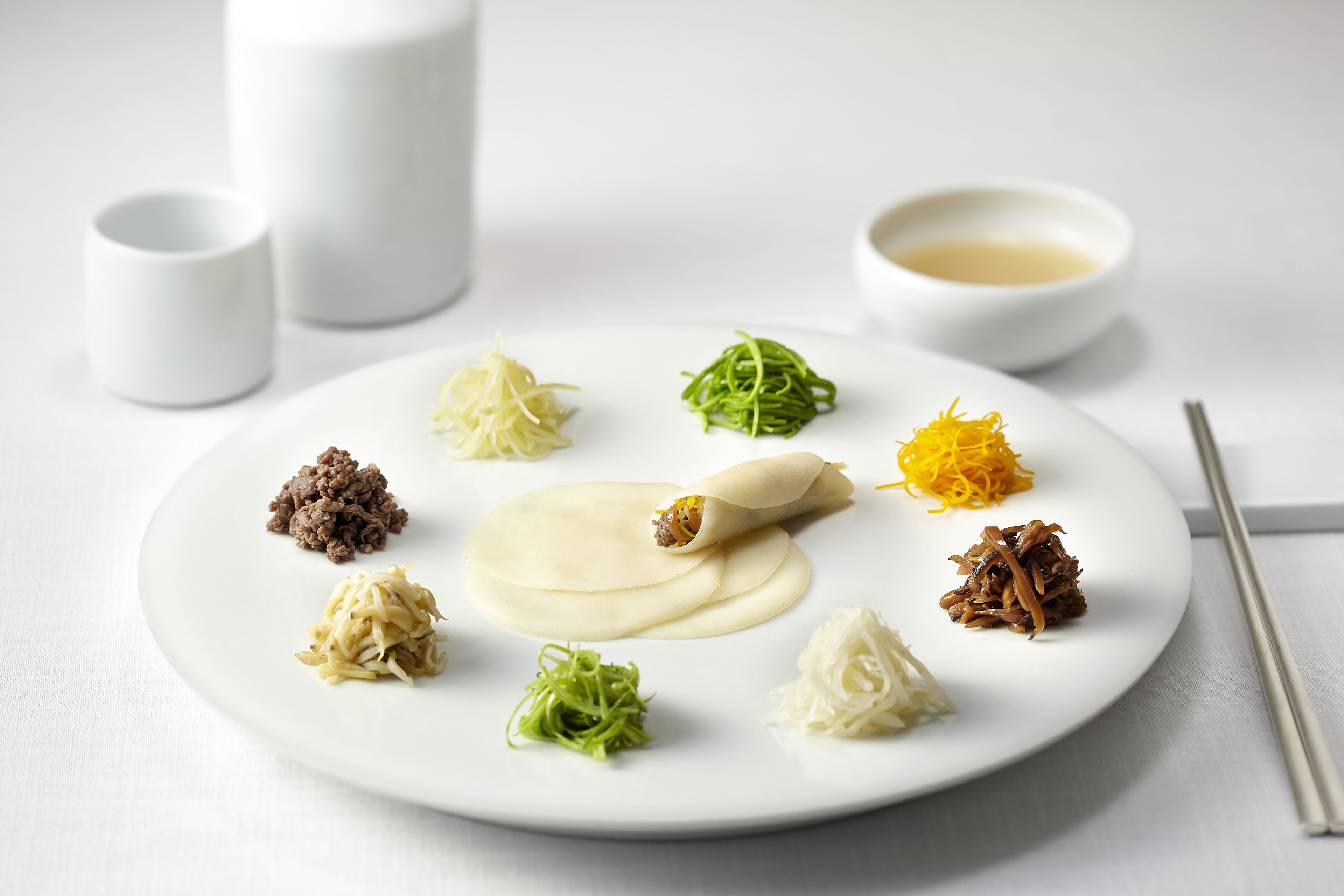 Un plato blanco con diversos alimentos y un par de palillos sobre una mesa.