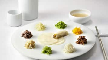 Un plato blanco con diversos alimentos y un par de palillos sobre una mesa.