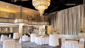 A spacious banquet hall with tiered seating, a grand chandelier, and a decorative cake centerpiece. - Hilton Long Island/Huntington (Melville)