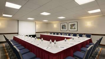 A conference room with a long table, chairs, and a projector screen.