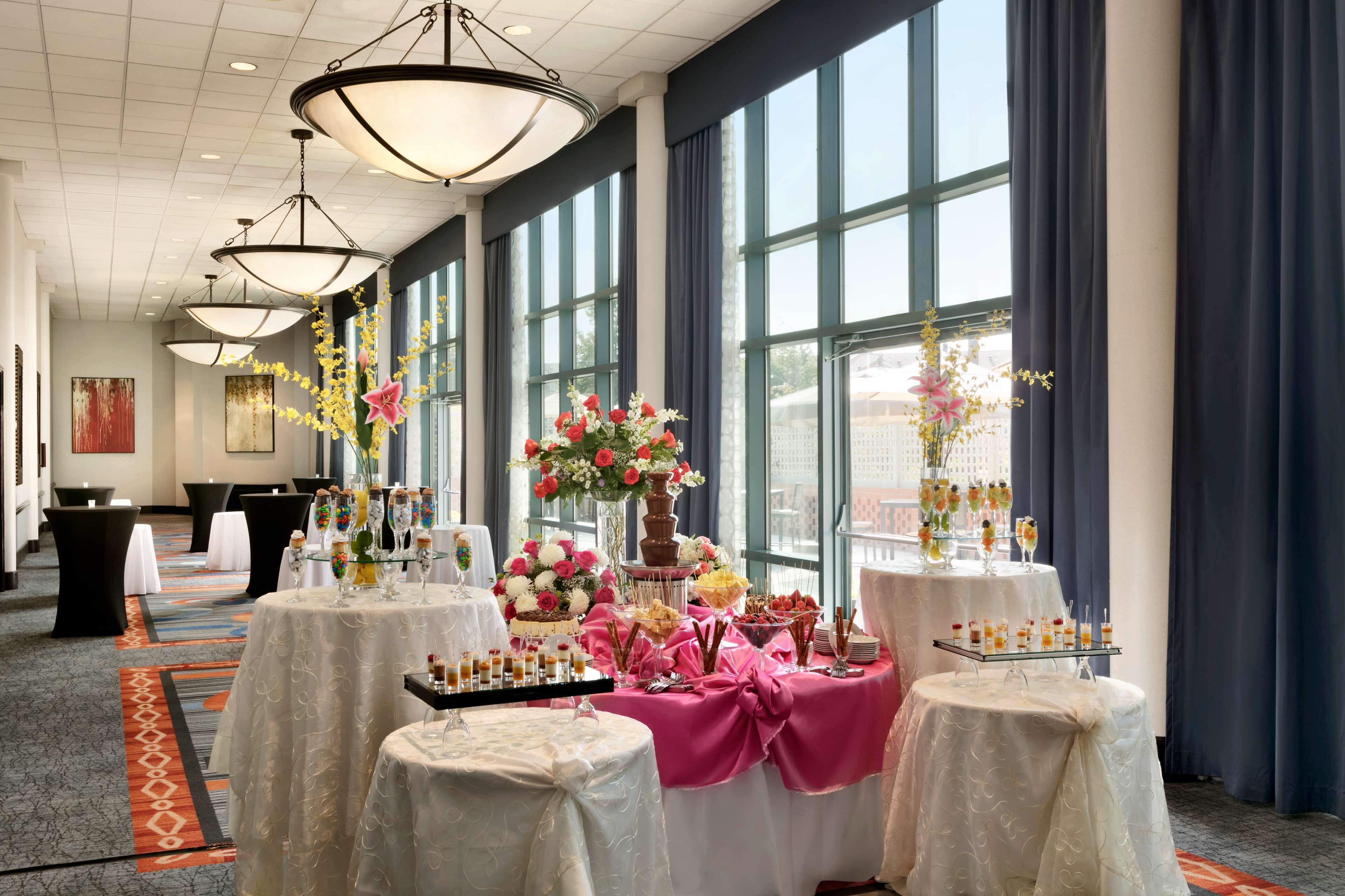 Une salle de banquet avec des tables rondes recouvertes de nappes blanches, agrémentées de compositions florales, et offrant un large choix de plats et de boissons.
