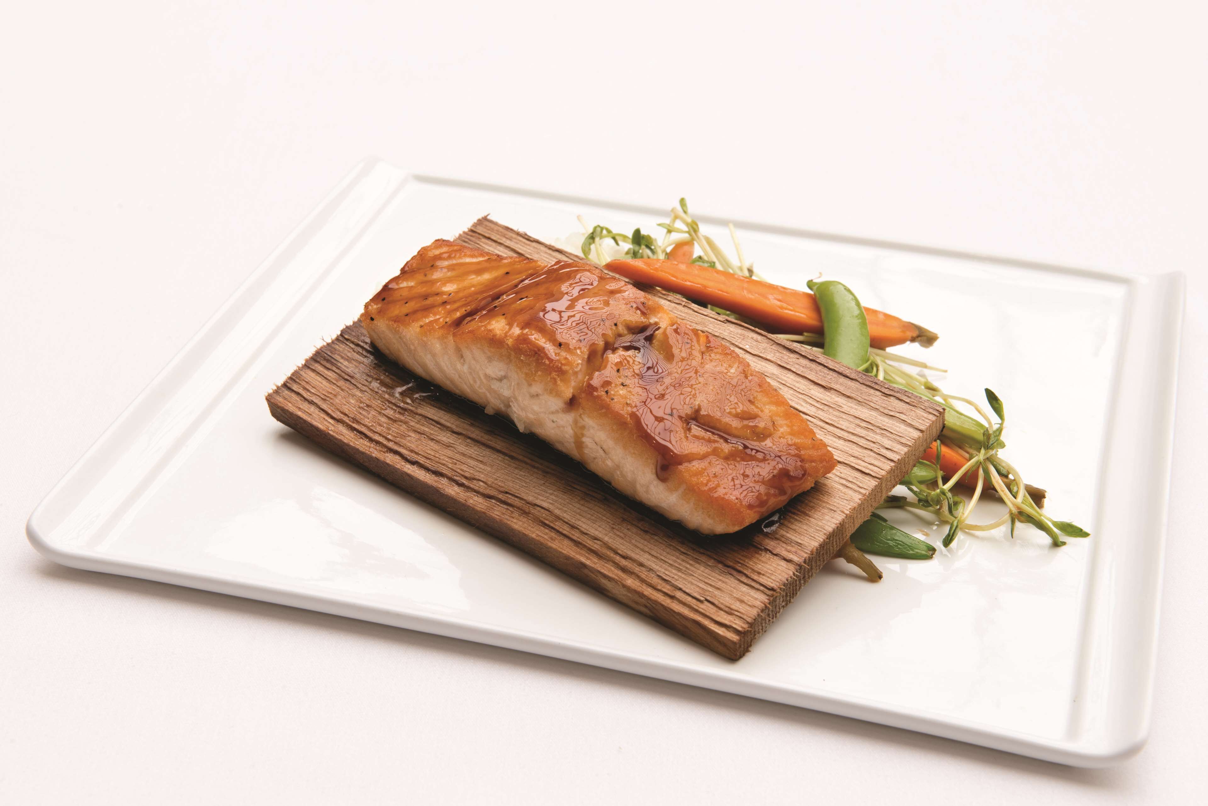 A piece of grilled salmon on a wooden board with a white plate.