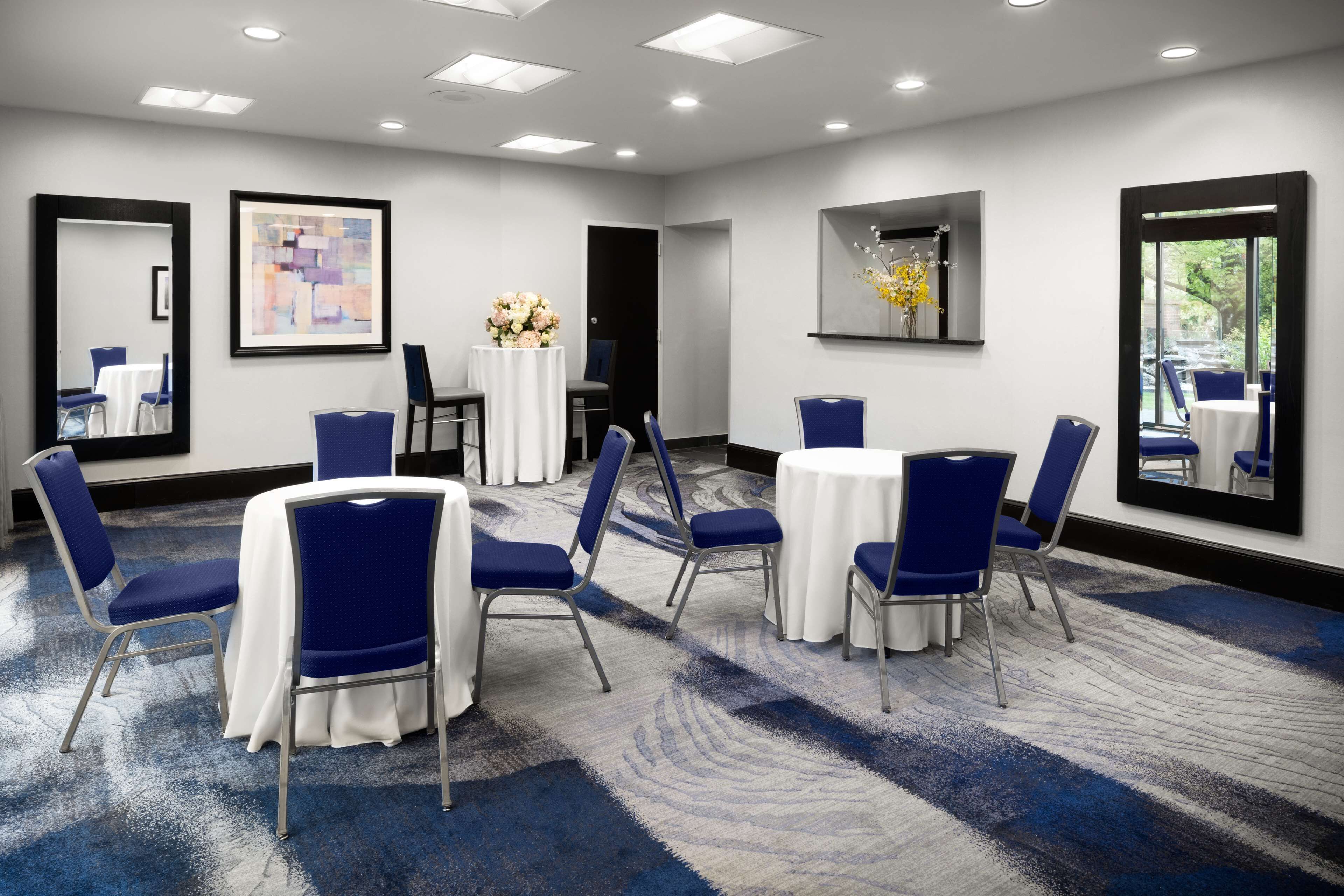 Un salón de conferencias con mesas redondas, sillas azules y manteles blancos.