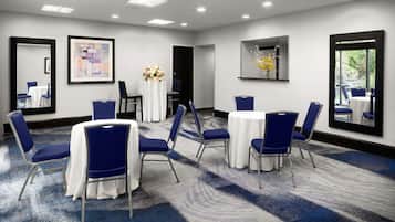 Un salón de conferencias con mesas redondas, sillas azules y manteles blancos.