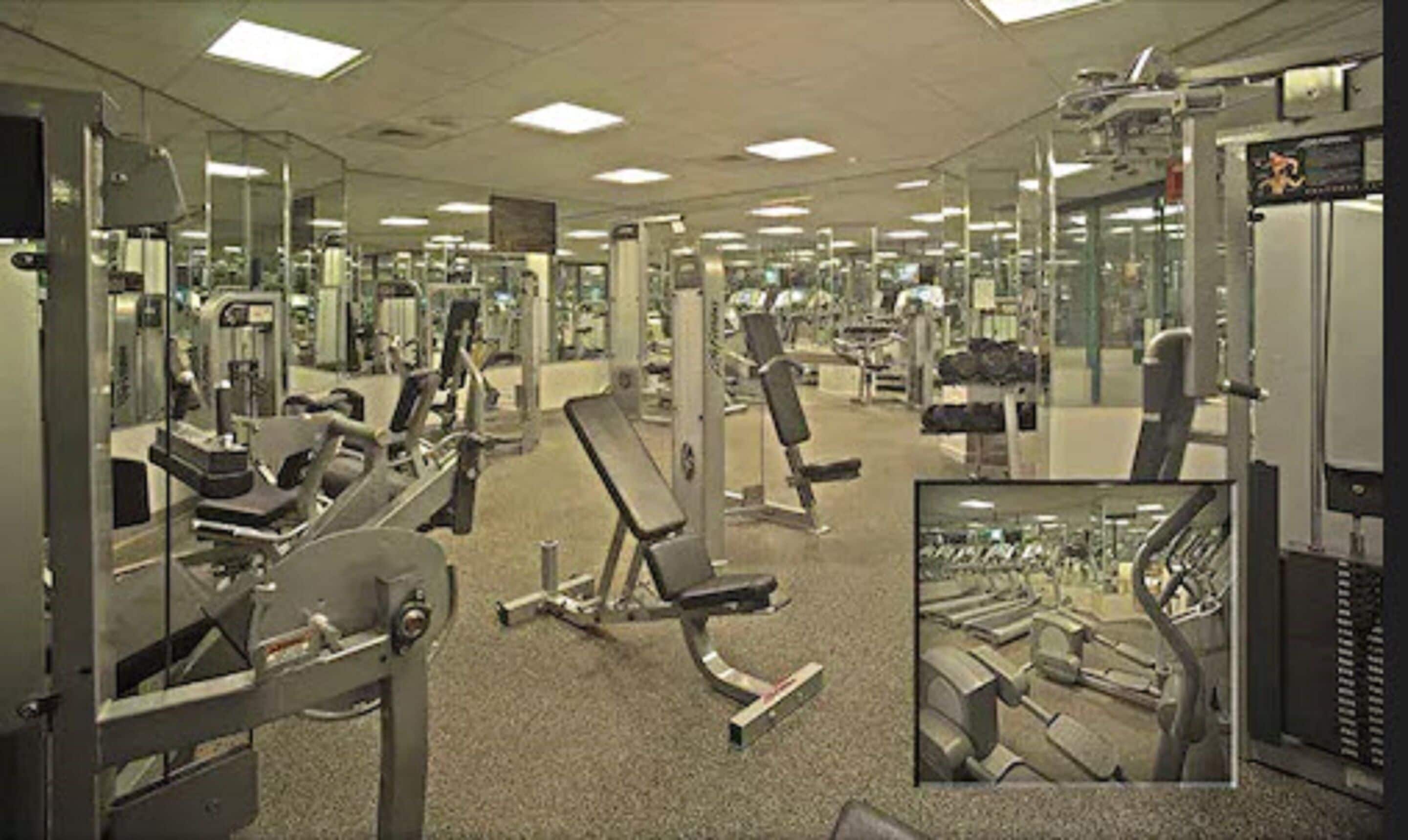 A gym with various exercise machines, mirrors, and a carpeted floor.