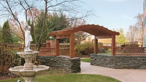 A garden with a stone fountain, a statue, and a wooden pergola. - Hilton Long Island/Huntington (Melville)